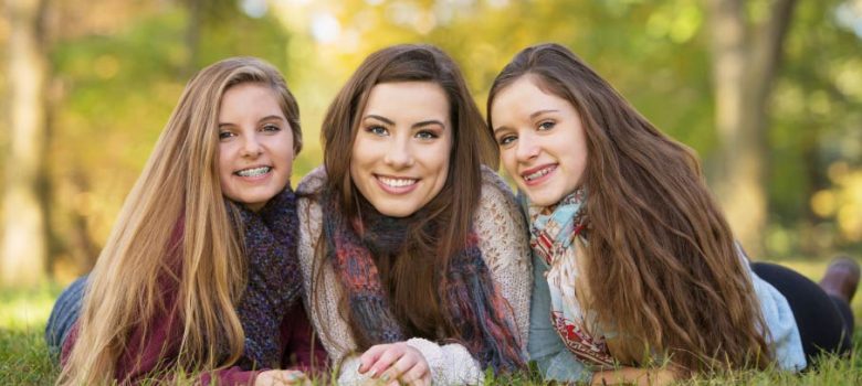three girls wearing scarves, two wearing braces, lying in grass and smiling